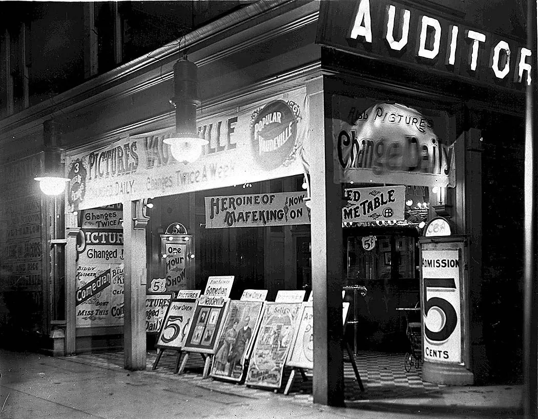 A theater front at night in Toronto, lit by lamps. Signs say pictures, vaudeville, one hour show, admission five cents.