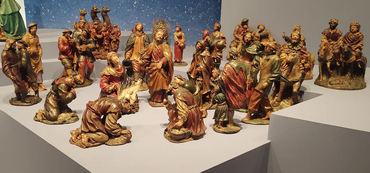 Dozens of small painted clay figures stand and kneel around a mother and her baby: shepherds, a man with a guitar, kings on horses and three camels.